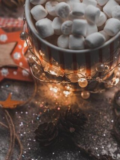 A cup of hot chocolate with small marshmallows is placed on a festively decorated table. Around the cup, lights and Christmas decorations are arranged. | © Pixabay