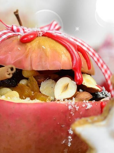 Ein dekorierter Apfel, gefüllt mit Nüssen und Trockenfrüchten, steht festlich auf einem goldenen Hintergrund. Rot-weiße Schleifen und ein Plätzchen in Sternform ergänzen die weihnachtliche Stimmung. | © Marktgemeinde Maria Lankowitz