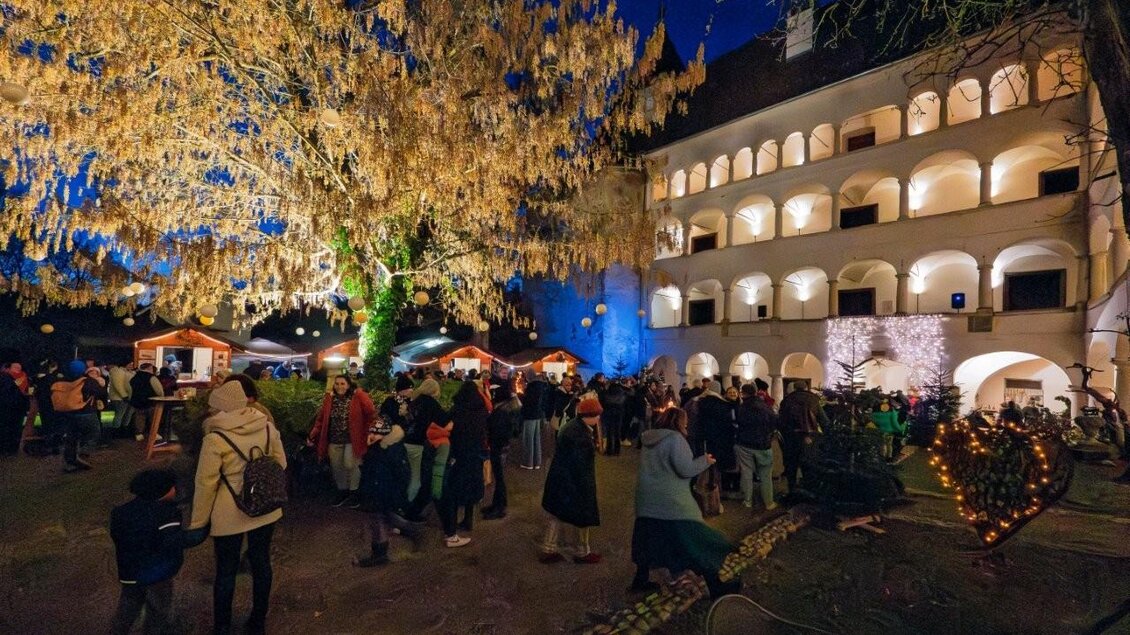 Ein festlicher Abend im Freien mit vielen Menschen und geschmückten Buden. Im Hintergrund ist ein historisches Gebäude und ein großer, beleuchteter Baum zu sehen. | © Günter Simmerl