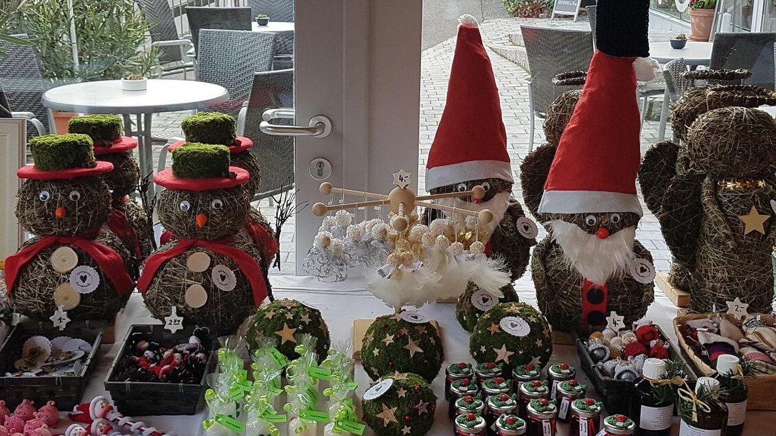 Auf dem Tisch sind festlich dekorierte Figuren in Form von Eulen mit Weihnachtsmütze und -schal zu sehen. Außerdem gibt es verschiedene handgemachte Kerzen und weitere dekorative Artikel. | © Vinothek Klöch - WBV Klöch