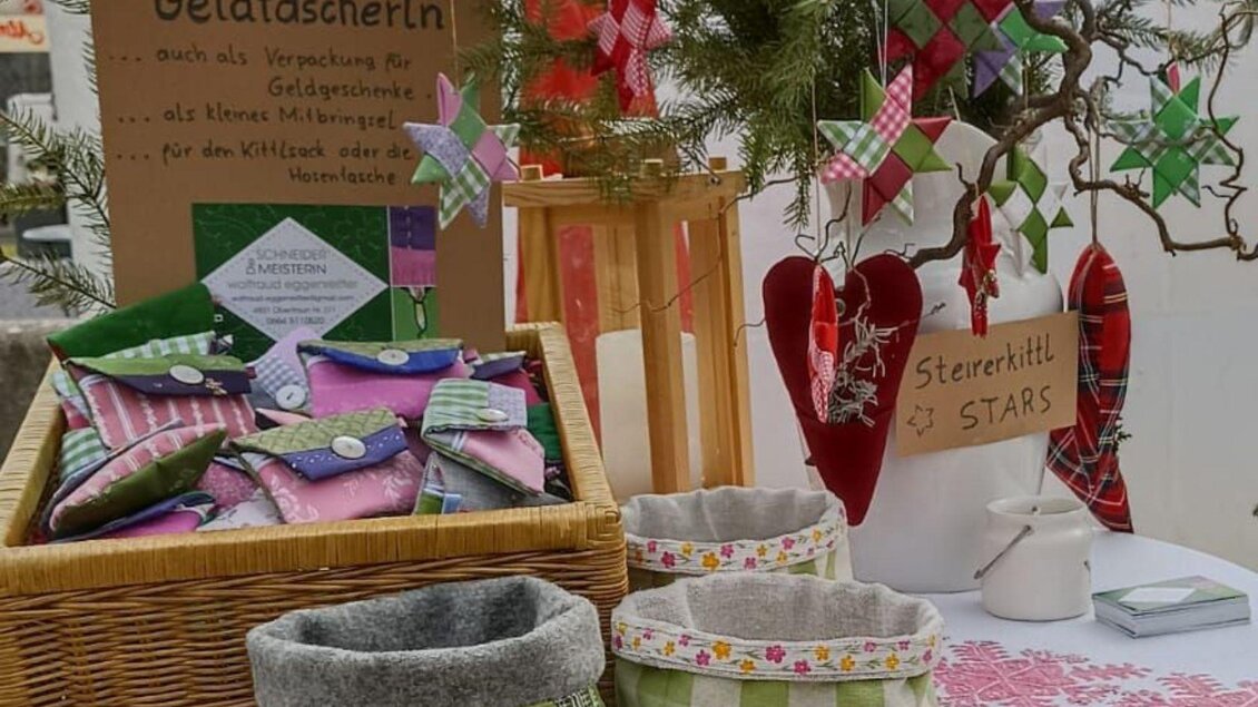 Ein Tisch mit handgefertigten Geldtaschen und dekorativen Sternen aus Papier. Im Hintergrund steht ein Schild mit der Aufschrift "Geldtascherln" und "Steirerhitl STARS". | © Waltraud Eggenreitter