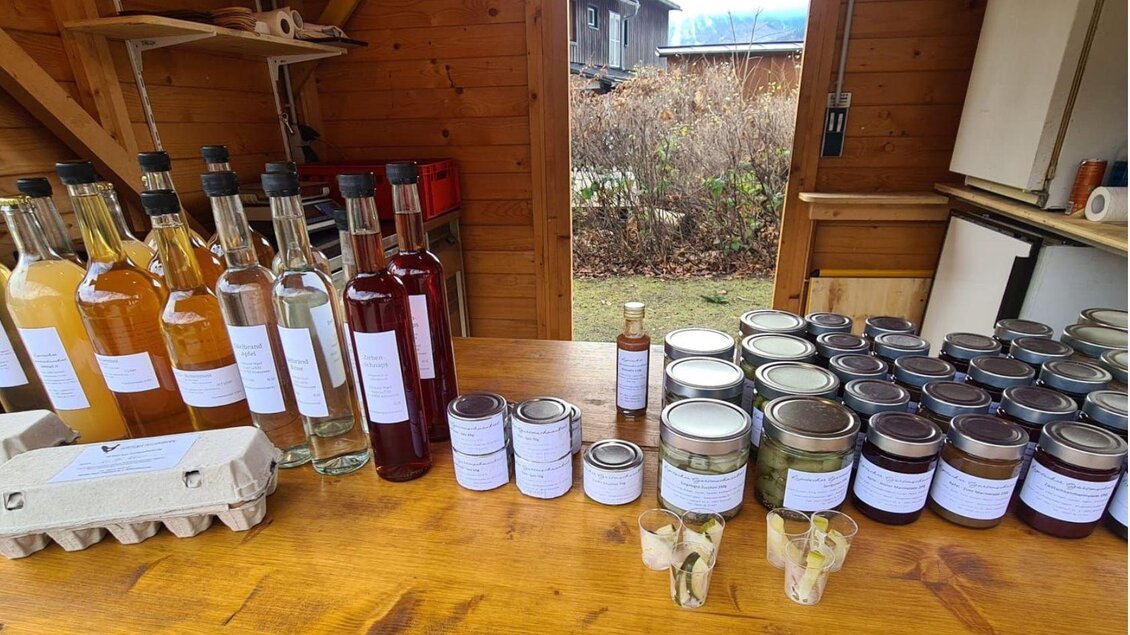 Ein Tisch in einer Holzscheune mit verschiedenen Flaschen von Säften und Likören sowie vielen gläsernen Einmachgläsern. Die Produkte sind gut etikettiert und zeigen eine Auswahl an selbstgemachten Lebensmitteln. | © Winfried Büttner
