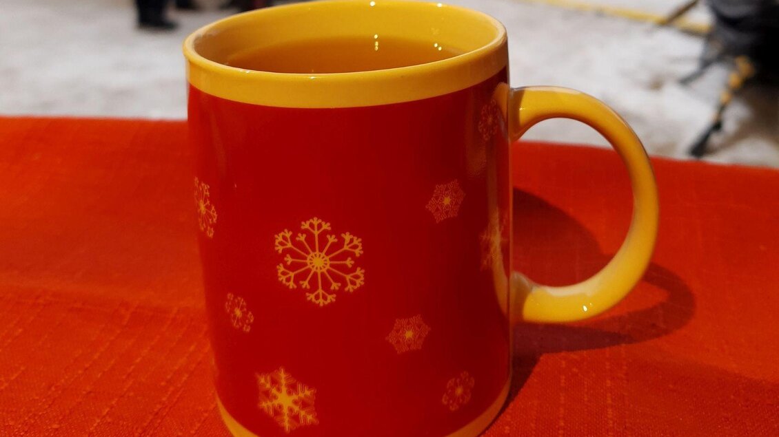 Eine rot-gelbe Tasse mit Schneeflocken-Muster steht auf einem Tisch. Der Inhalt der Tasse sieht nach warmem Getränk aus. | © Bettina Illmayer