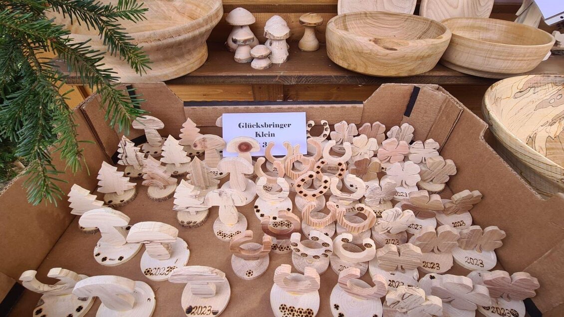 Eine Auswahl handgefertigter Holzfiguren in verschiedenen Formen und Größen liegt in einem Karton. Im Hintergrund sind weitere Holzschalen zu sehen. | © Winfried Büttner