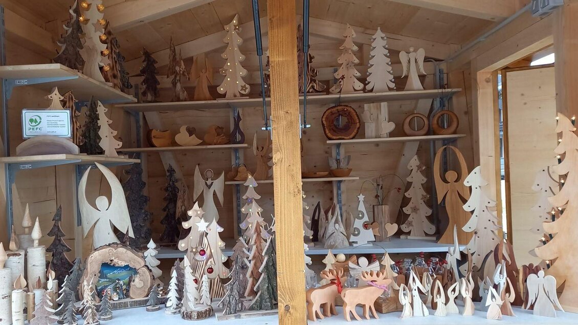 Ein Holzstand voller handgefertigter Figuren und Weihnachtsbäume. Die Dekorationen variieren in Form und Größe und strahlen eine gemütliche, festliche Atmosphäre aus. | © Eva Kalkgruber