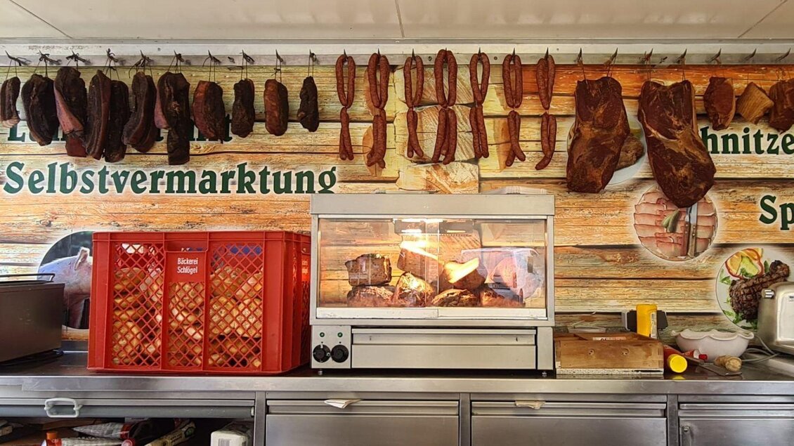 Eine Fleischerei mit verschiedenen Wurst- und Fleischsorten, die an der Wand hängen. Im Vordergrund steht ein Fleischgrill, der die Produkte präsentiert. | © Winfried Büttner