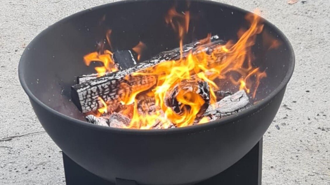 Ein runder Feuerkorb mit brennendem Holz und lebhaftem Feuer. Die Flammen tanzen und erzeugen eine warme, einladende Atmosphäre. | © Winfried Büttner