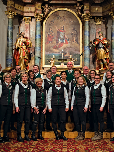 A group of singers stands in a church in front of a beautiful altar. All members are dressed festively and smile at the camera. | © Gemischter Chor Bad Loipersdorf