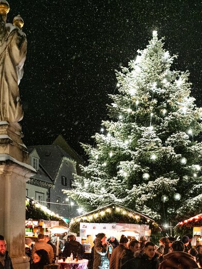 A festive Christmas market with a large, decorated Christmas tree in the snow. Many people enjoy the atmosphere and the stalls of market vendors. | © Tourismusverband Südsteiermark