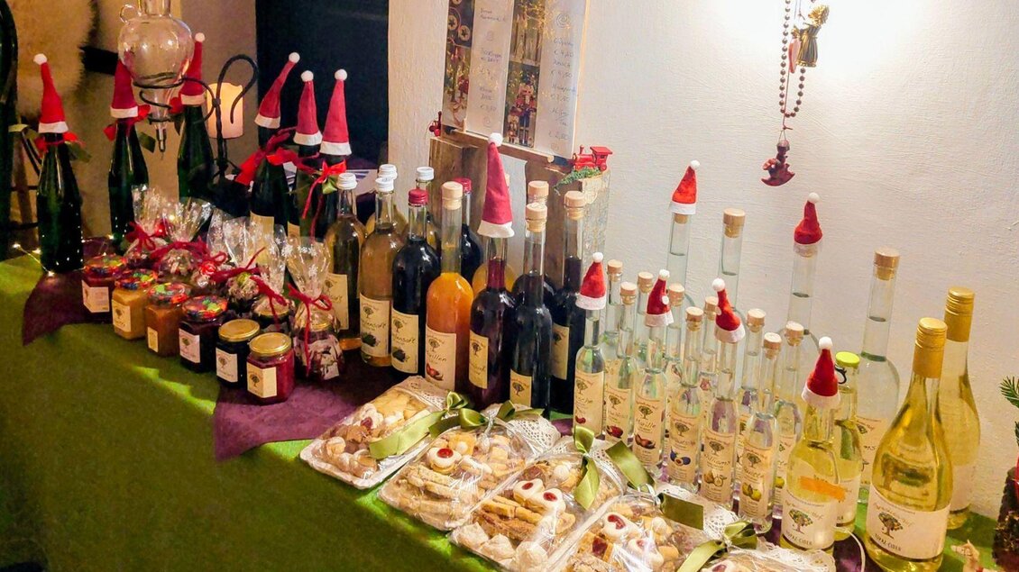 Ein festlich dekorierter Tisch mit verschiedenen Flaschen und Gläsern. Viele Produkte tragen kleine Weihnachtsmann-Mützen und es gibt auch einige Leckereien. | © Podenhaus, Bad Aussee