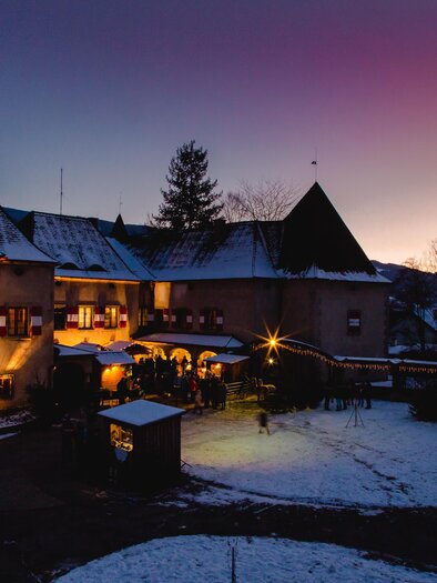 Ein charmantes Schloss mit Türmen, das in der Dämmerung beleuchtet ist. Schneebedeckte Landschaft und ein klarer Himmel runden die winterliche Atmosphäre ab. | © TV Hochsteiermark