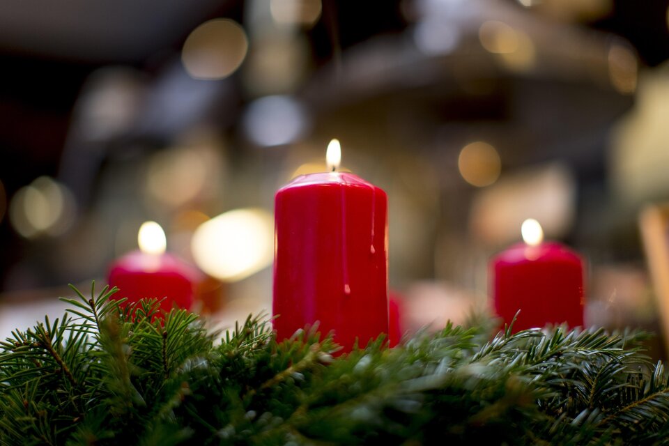 Rote Kerzen brennen auf einem Adventskranz aus Tannenzweigen. Hintergrund mit unscharfen Lichtpunkten erzeugt eine festliche Stimmung. | © Tom Lamm