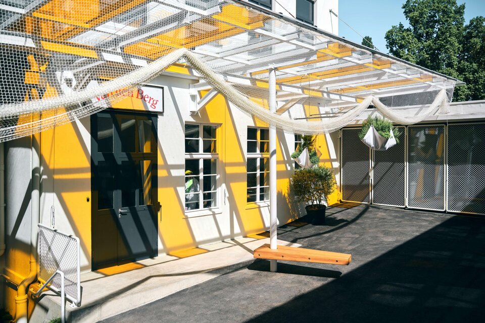 Innenhof des Van den Berg in Graz mit gelber Fassade, Netzinstallationen und überdachtem Außenbereich. | © Stefan Leitner