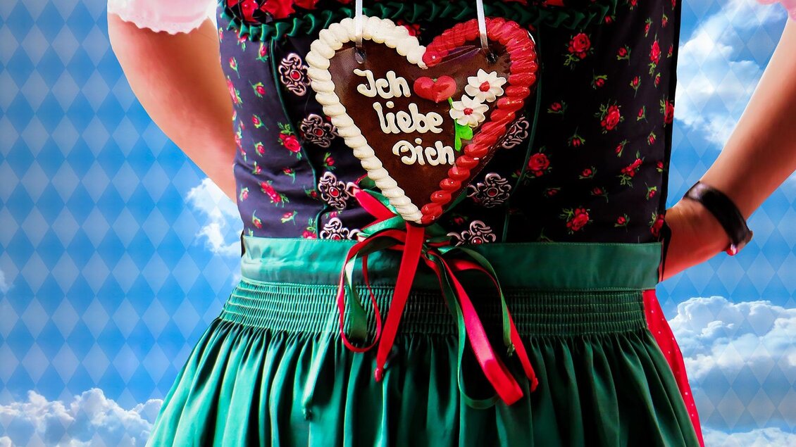 Eine Frau trägt ein traditionelles Dirndl mit einem Lebkuchenherz, auf dem „Ich liebe Dich“ steht. Der Hintergrund zeigt einen klaren Himmel mit Wolken. | © Symbolfoto Pixabay