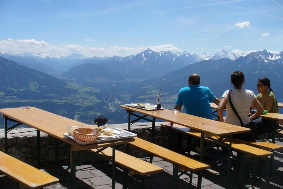 Eine Gruppe von Menschen sitzt an einem Tisch mit Blick auf die Berge. Die sonnige Landschaft zeigt schneebedeckte Gipfel und ein weites Tal. | © Pixabay