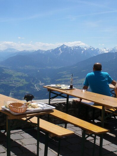 Eine Gruppe von Menschen sitzt an einem Tisch mit Blick auf die Berge. Die sonnige Landschaft zeigt schneebedeckte Gipfel und ein weites Tal. | © Pixabay