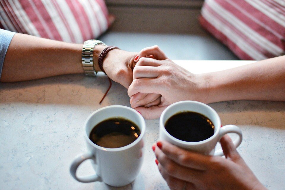 Zwei Personen halten sich in einem Café die Hände. Vor ihnen stehen zwei Tassen Kaffee auf einem Tisch. | © Pixabay