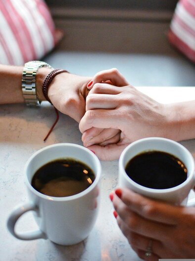 Zwei Personen halten sich in einem Café die Hände. Vor ihnen stehen zwei Tassen Kaffee auf einem Tisch. | © Pixabay