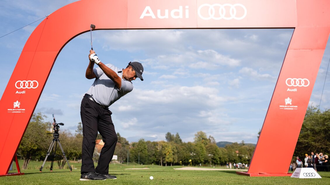 Ein Golfer schlägt vor einem großen Audi-Bogen auf einem Golfplatz ab. Im Hintergrund sind Zuschauer und ein klarer Himmel zu sehen. | © GEPApictures