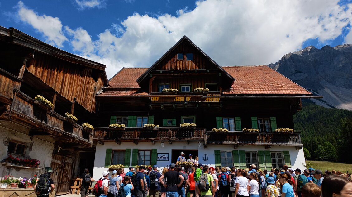 Eine große Menschenmenge vor einem traditionell gestalteten Gebäude in den Bergen. Der Himmel ist blau mit einigen Wolken, und die Umgebung ist grün und naturnah. | © Tourismusverband Schladming-Dachstein