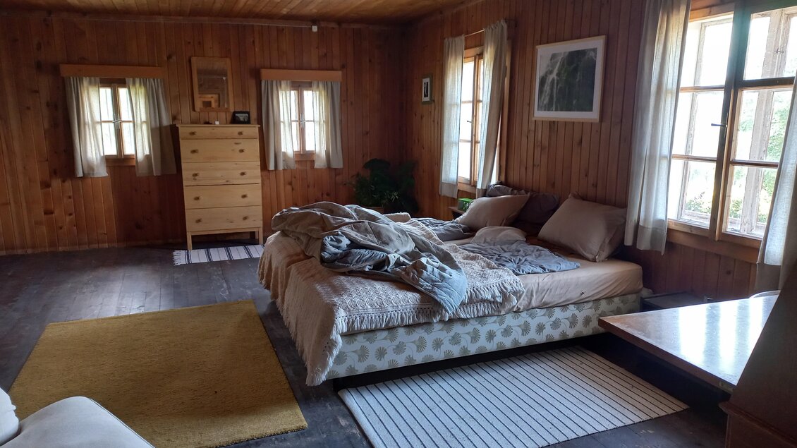 Ein gemütliches Zimmer mit Holzverkleidung und großen Fenstern. Ein Bett mit Decken und eine Kommode sind sichtbar. | © Tourismusverband Schladming-Dachstein