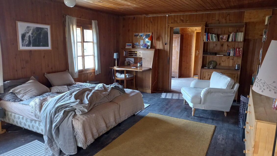 Ein gemütliches Schlafzimmer mit Holzverkleidung, einem großen Bett und einem Sessel. Das Zimmer hat einen warmen, einladenden Charakter und ist gut eingerichtet. | © Tourismusverband Schladming-Dachstein