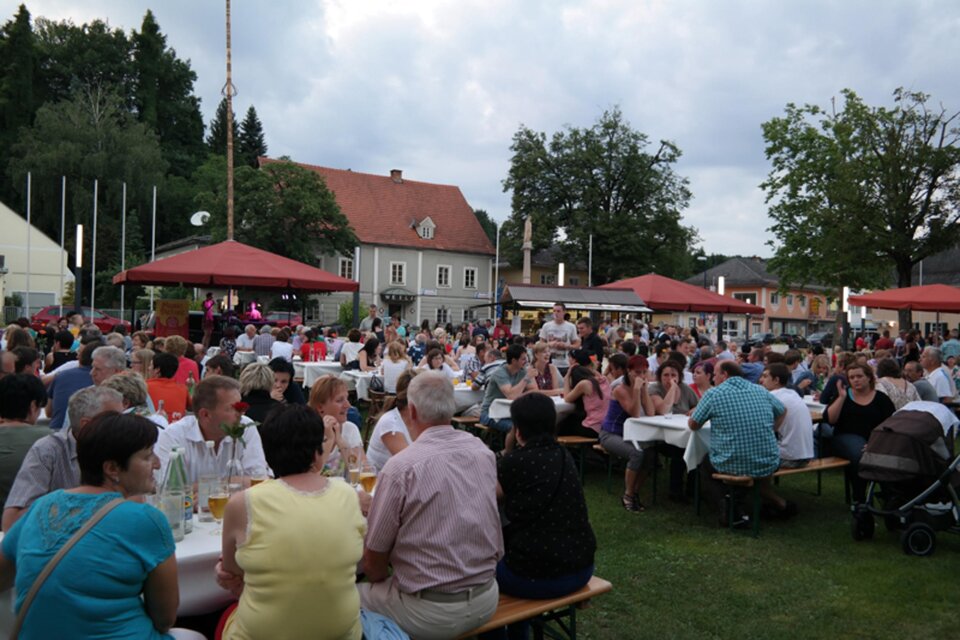 Eine belebte Veranstaltung im Freien mit vielen Menschen, die an Tischen sitzen. Im Hintergrund sind Pavillons und Bäume zu sehen. | © Wieser Weinbauern