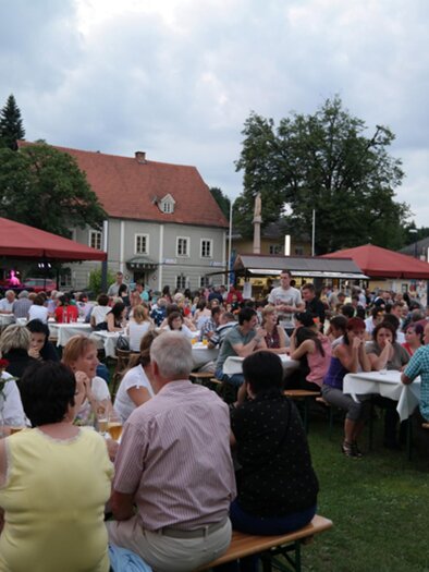 Eine belebte Veranstaltung im Freien mit vielen Menschen, die an Tischen sitzen. Im Hintergrund sind Pavillons und Bäume zu sehen. | © Wieser Weinbauern