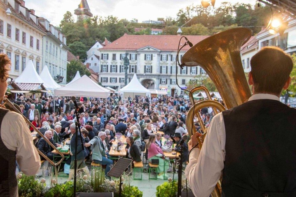 Ein lebhaftes Stadtfest mit vielen Menschen, die an Tischen sitzen und Musik genießen. Im Vordergrund spielen zwei Musiker auf der Bühne. | © TV Thermen- Vulkanland