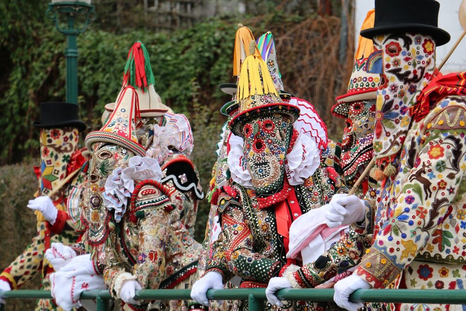 Die Ausseer Flinserl in ihren aufwendigen, bunt bestickten Kostümen und Masken stehen an einem Geländer in der Mitte von Bad Aussee. Die festliche Atmosphäre ihres traditionellen Umzugs zum Ausseer Fasching ist deutlich spürbar. | © TVB Ausseerland - Theresa Schwaiger