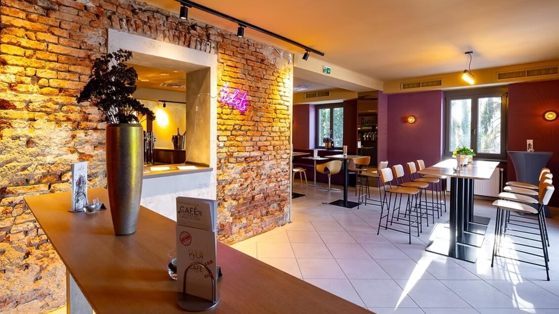 Innenraum des Café Marie mit Backsteinwand, Hochtischen und Sitzplätzen als Ausstellungsort in Eggersdorf. | © Cafè Marie