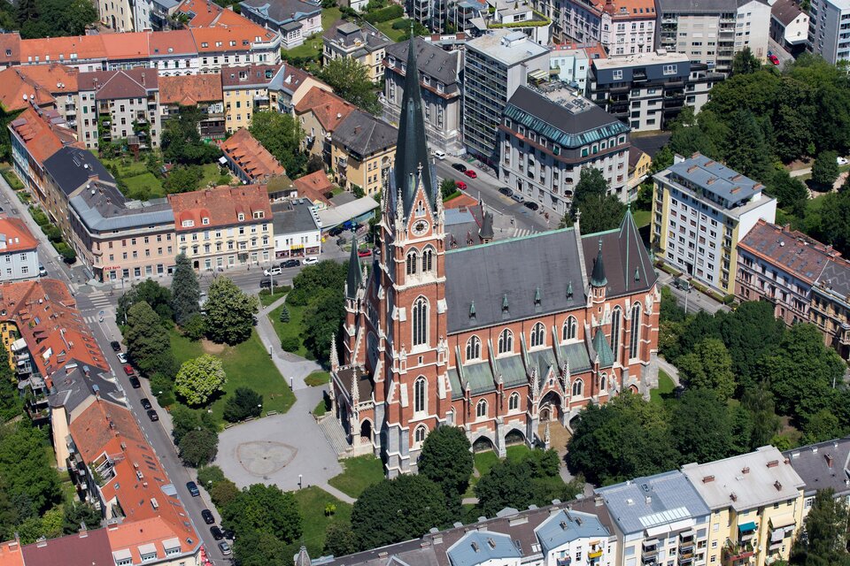 Eine beeindruckende Kirche im gotischen Stil steht umgeben von Stadtgebäuden. Die bunten Dächer der umliegenden Häuser schaffen einen schönen Kontrast zur Architektur der Kirche. | © Graz Tourismus-Harry Schiffer