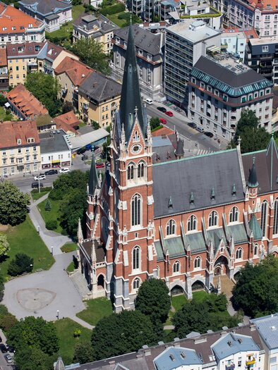 An impressive church in Gothic style stands surrounded by city buildings. The colorful roofs of the surrounding houses create a beautiful contrast to the architecture of the church. | © Graz Tourismus-Harry Schiffer