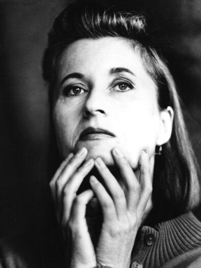 A black-and-white portrait of a woman with a thoughtful expression. She is holding her face with both hands and looking upwards. | © Vukovits