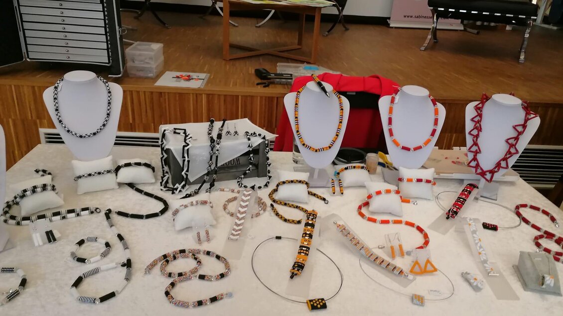 Ein Tisch mit einer Auswahl an Schmuckstücken, darunter Halsketten und Armbänder in verschiedenen Farben und Designs. Die Schmuckstücke sind auf Ständern ausgestellt und bestehen aus unterschiedlichen Materialien. | © Susanne Braun