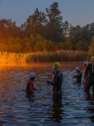 Triathleten im Neoprenanzug beim Schwimmstart eines eXtreme Triathlons in Gössendorf bei Morgendämmerung. | © Region Graz-Gerald Hirl