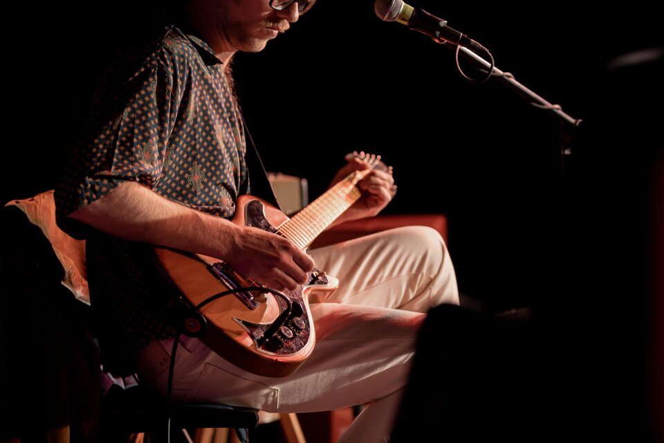 Ein Musiker spielt Gitarre auf der Bühne. Die Atmosphäre ist entspannt und die Beleuchtung ist gedämpft. | © TVB Südsteiermark – Achromatic Photography