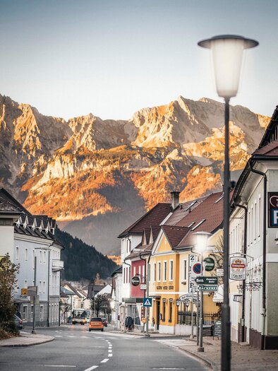 A quiet street with colorful buildings and a beautiful view of the mountains in the background. The scene radiates a warm atmosphere. | © Tourismusverband Gesäuse