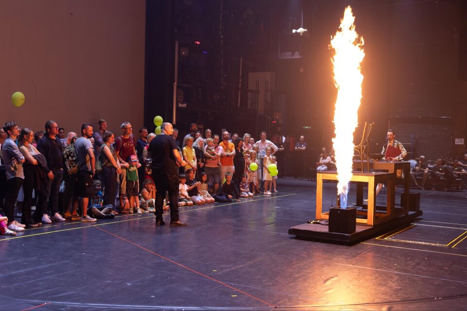 Eine große Menschenmenge sieht einer spektakulären Wissenschaftsdemonstration zu. Auf der Bühne gibt es ein Feuer, das aus einem Gerät heraus zündet. | © Oper Graz