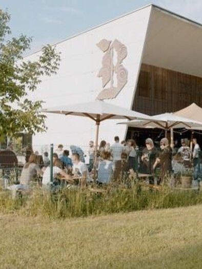 Ein modernes Café mit Außenbereich und vielen Gästen. Der Raum ist von einer grünen Wiese und Bäumen umgeben. | © Brauhaus Bevog