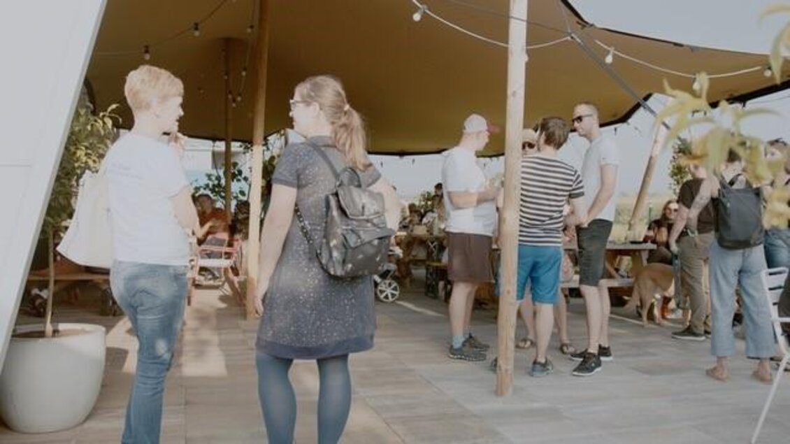 Eine lebhafte Veranstaltung im Freien mit vielen Menschen, die miteinander sprechen. Es gibt Tische und eine einladende Atmosphäre unter einem großen Sonnensegel. | © Brauhaus Bevog