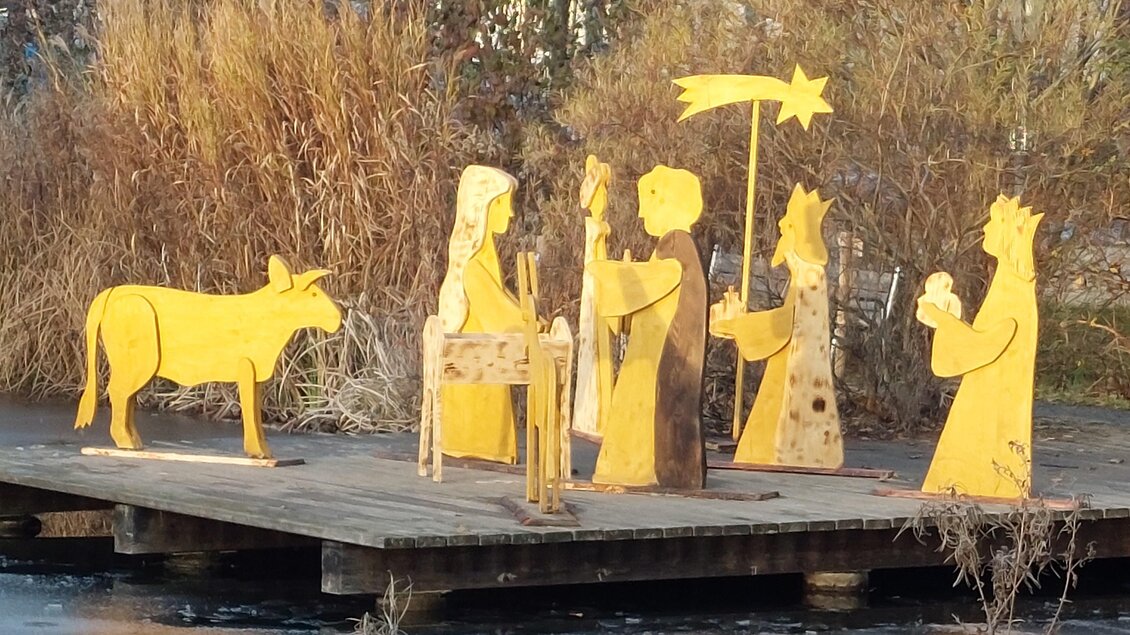 Eine bunte Krippe aus Metallfiguren steht auf einem Holzsteg. Die Figuren stellen die Heilige Familie und einige Tiere dar. | © Lederer