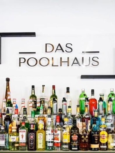 Eine Bar mit einer Vielzahl von Getränken und alkoholischen Spirituosen. Über der Bar hängt das Schild "DAS POOLHAUS". | © Dominik Wolf
