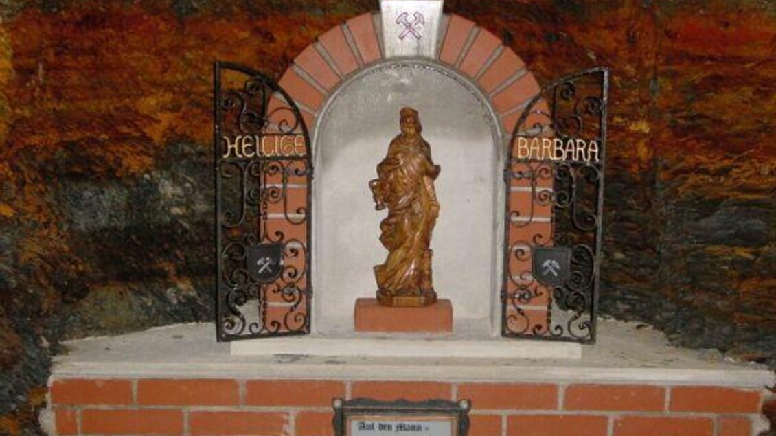 Eine Statue der heiligen Barbara ist in einer Nische mit einem dekorativen Gitter untergebracht. Der Raum hat eine rustikale Steinmauer und eine bescheidene, aber ehrwürdige Atmosphäre. | © Bergbauverein Öblarn