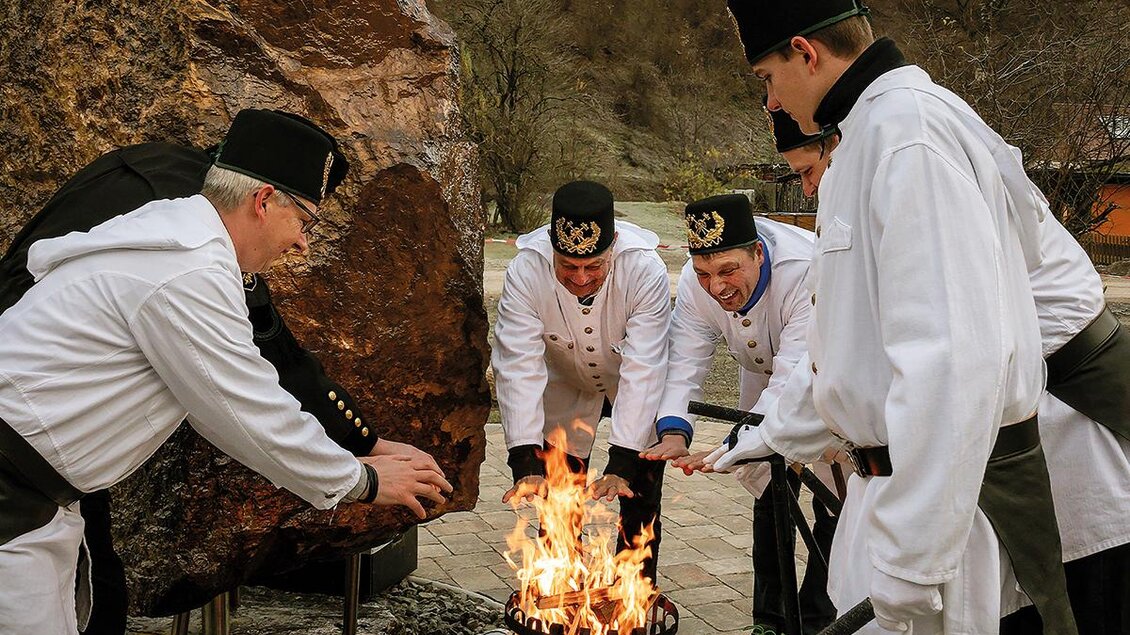 Sechs Personen in weißen Anzügen stehen um ein Feuer. Sie scheinen an einer Feier oder Tradition teilzunehmen. | © Norbert Schmidt