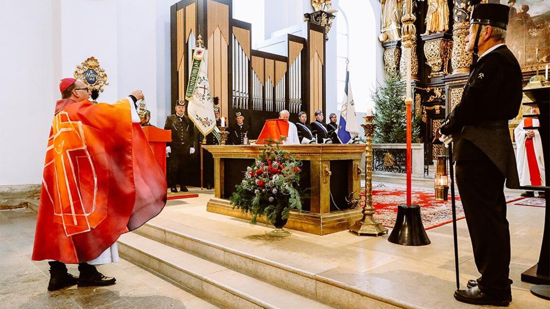 Eine feierliche Zeremonie in einer Kirche mit einem Kardinal, der am Altar spricht. Im Hintergrund sind beeindruckende Kirchenornamente und eine versammelte Gemeinde zu sehen. | ©  Foto Freisinger