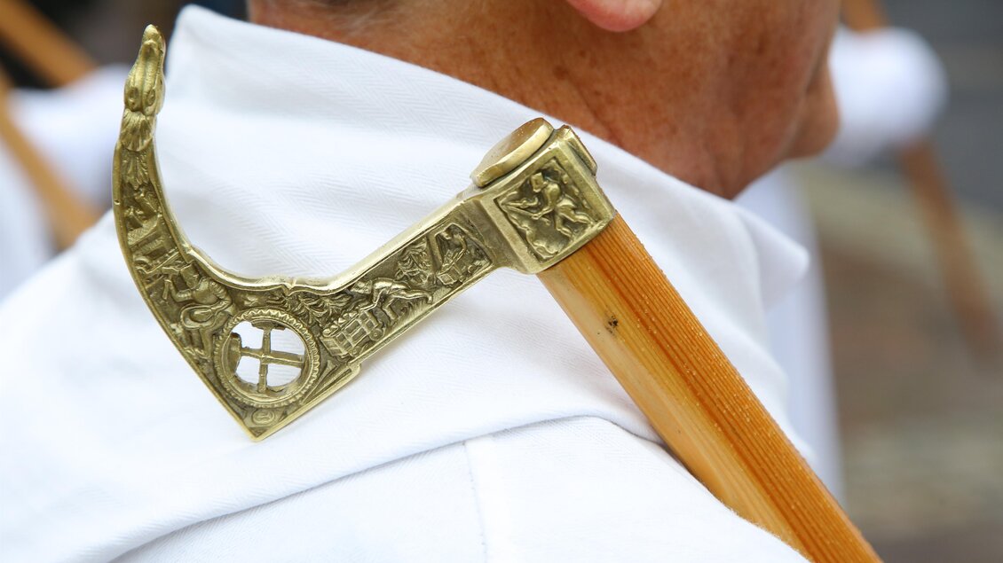Ein Detail einer historischen Zeremonie mit einem kunstvoll verzierten Stock. Der Stock ist an der Schulter einer Person befestigt, die ein weißes Gewand trägt. | © Freisinger