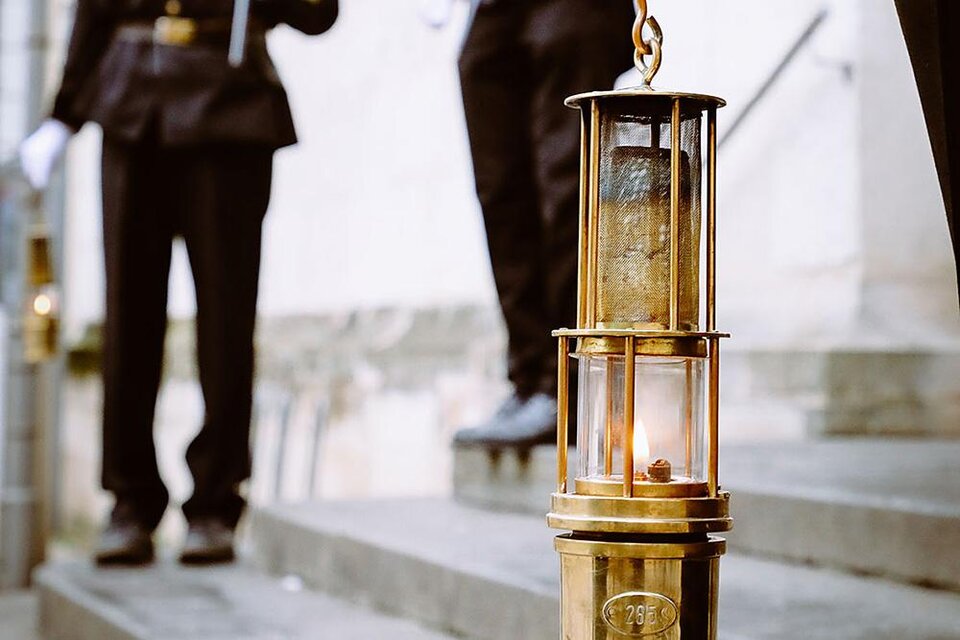 Eine historische Laterne steht auf einer Treppe, während im Hintergrund Personen in Uniformen zu sehen sind. Die Laterne brennt und verleiht der Szene eine feierliche Atmosphäre. | © Russold