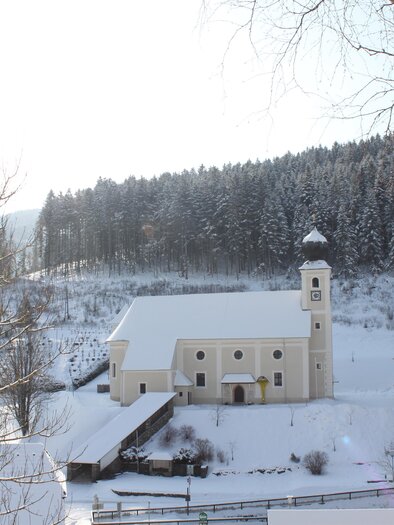 A snowy landscape with a pretty village and a church. In the background, there are trees covered with snow. | © Gemeinde Gasen