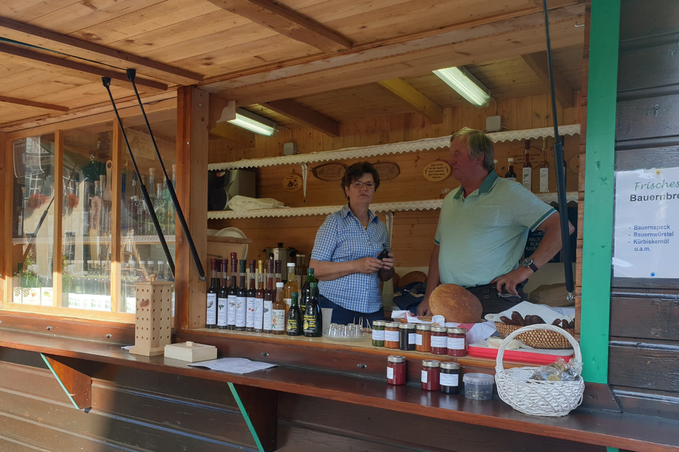 <p>Bauernmarkt bei dem frische Lebensmittel anbieten. Im Hintergrund sind verschiedene Flaschen und Produkte sichtbar.</p> | © Petra Hochlahner